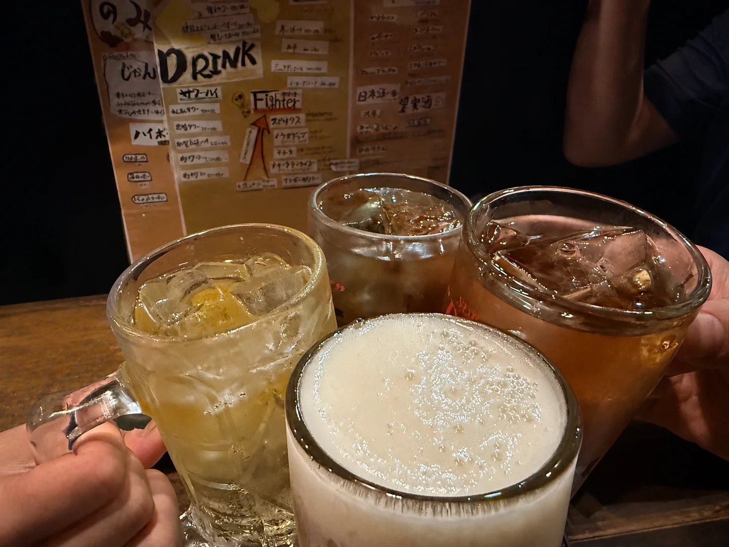 泡の立つ大きなジョッキを持ち上げる手元と木のテーブルに並ぶ小皿